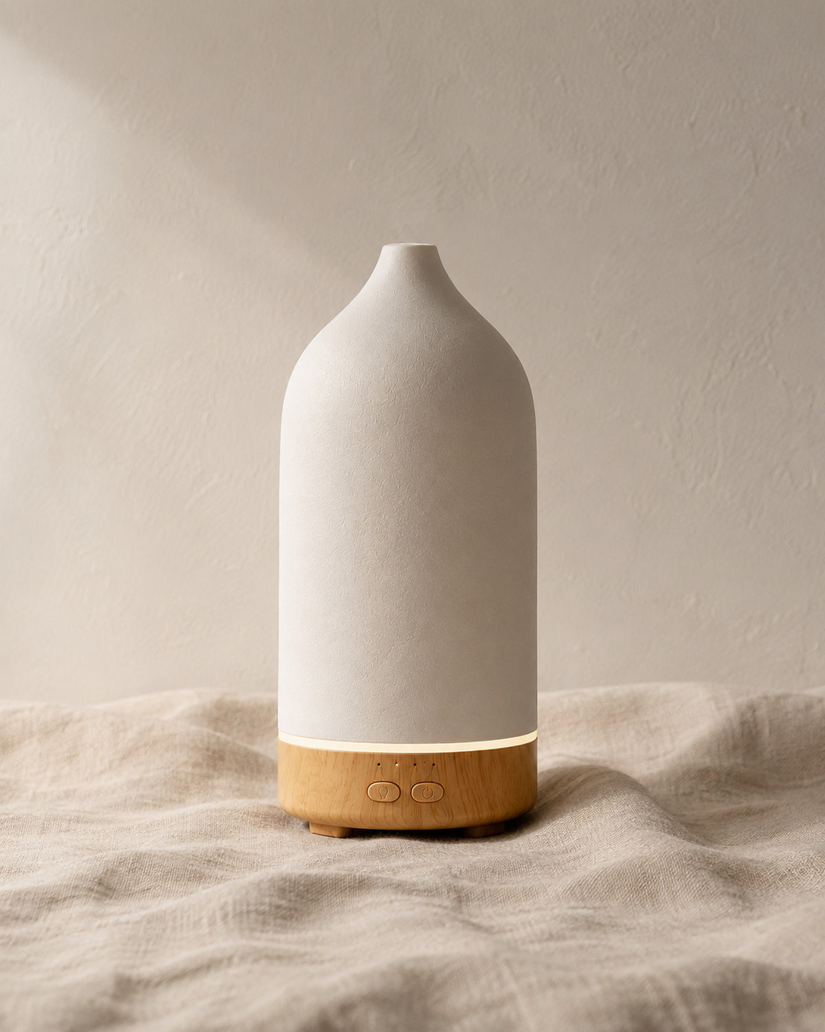 The diffuser standing on crumpled linen against a pale plaster wall